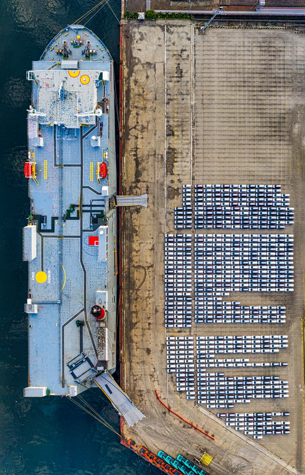 Car carrier ship docked beside rows of cars ready for export at port